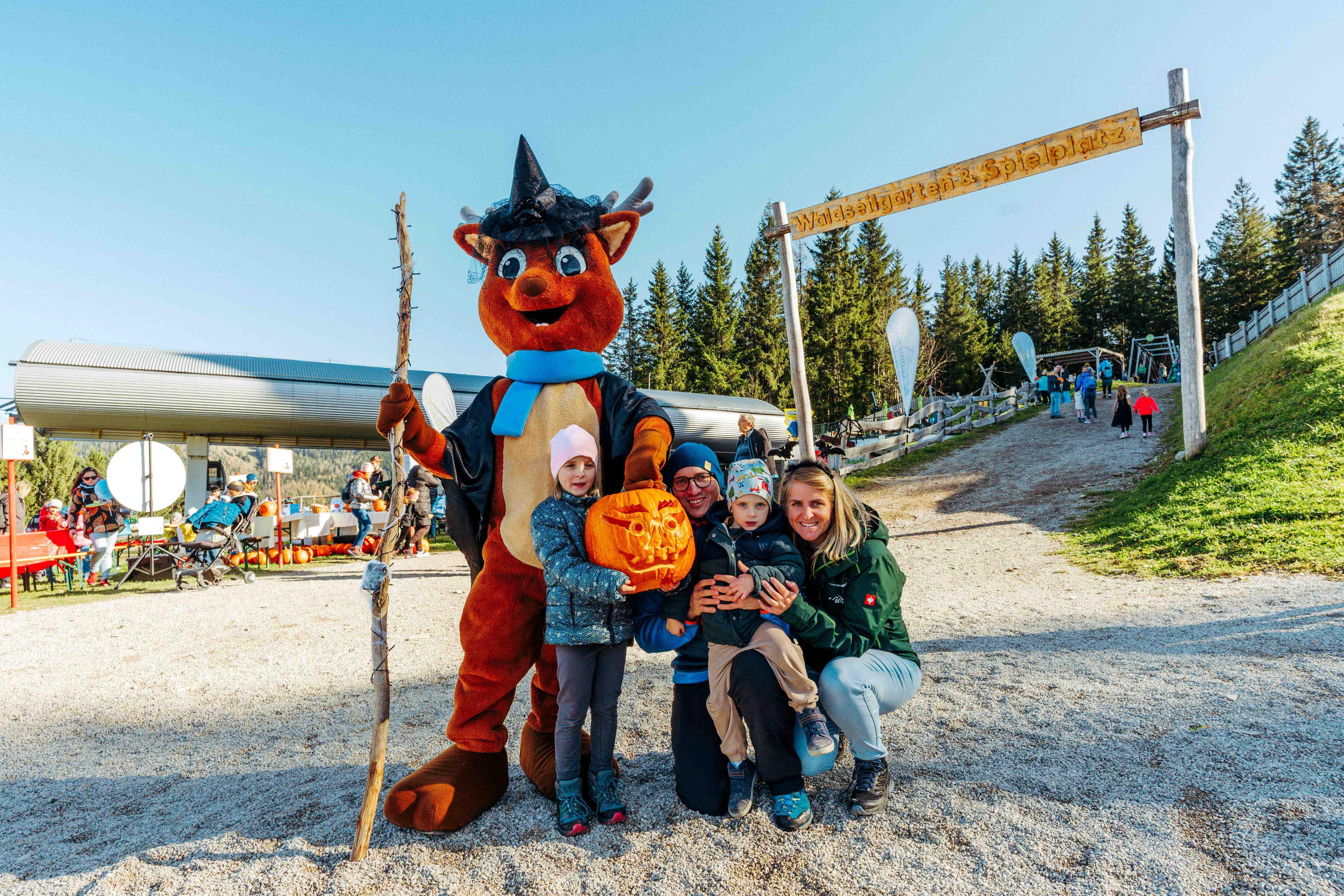Gruppenfoto einer Familie mit dem Maskottchen vom Semmering Hirschenkogel. Die Familie hält einen geschnitzten Kürbis in der Hand.