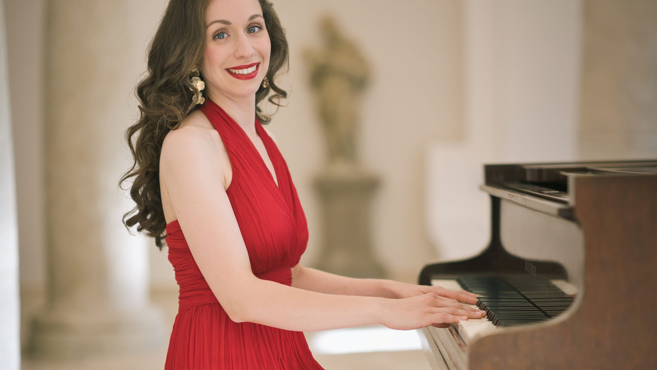 Foto einer Dame im roten Kleid, die an einem Klavier sitzt,