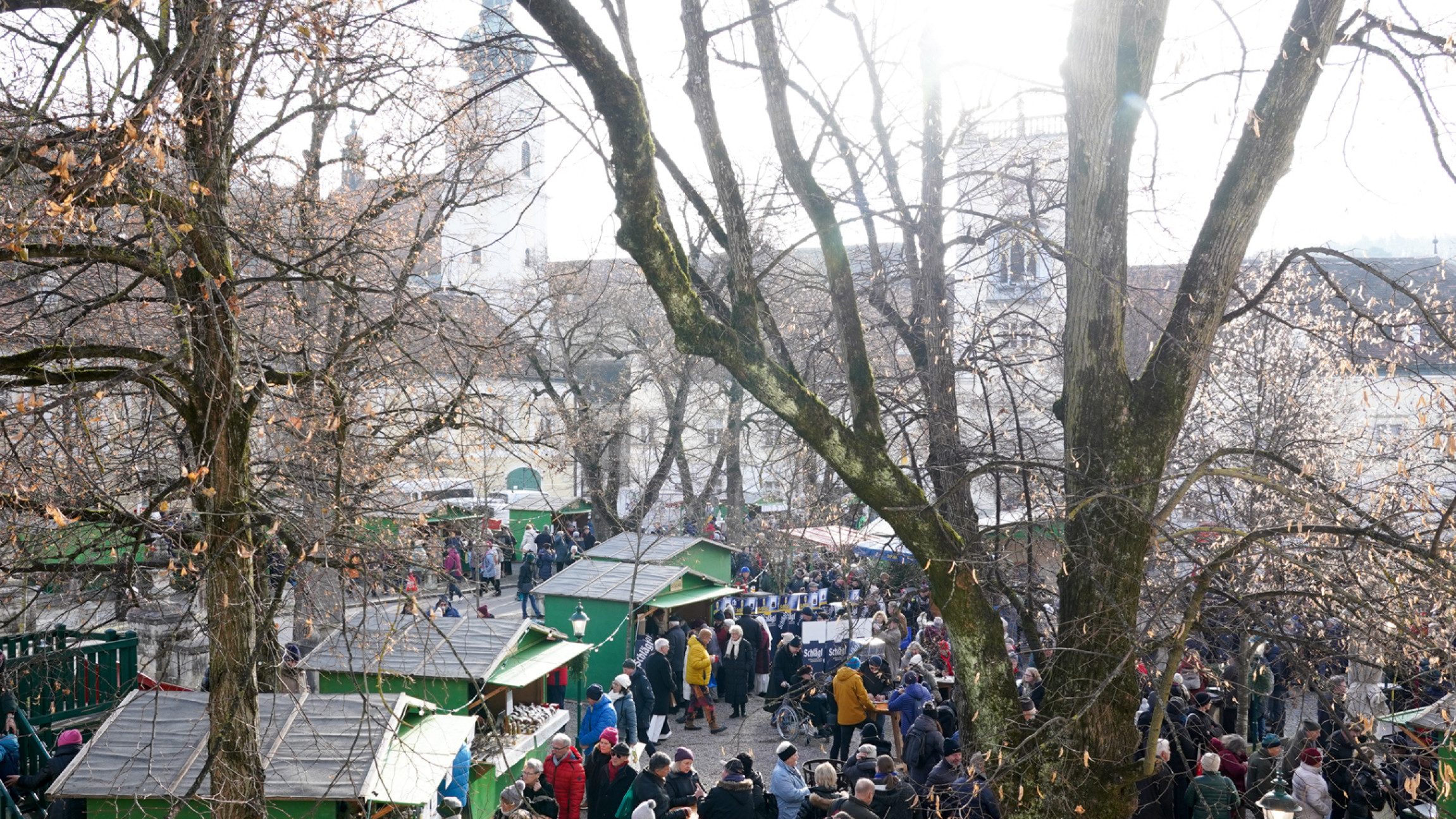 Blick von schräg oben auf mehrere kleine Holzhütten mit vielen Menschen davor.