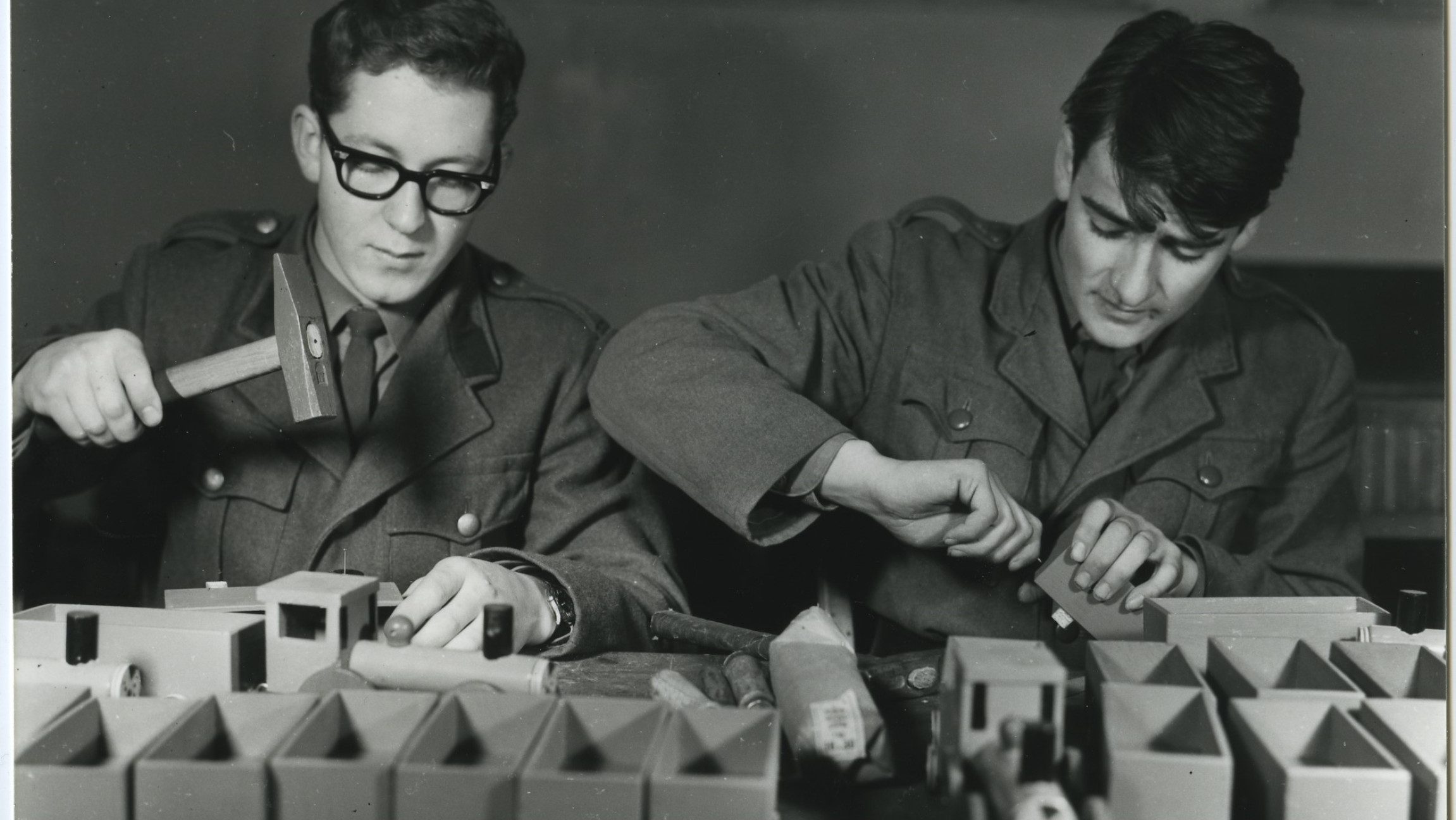 Schwarz-weiß Foto von zwei Männern in Uniform, die Spielzeug aus Holz herstellen.