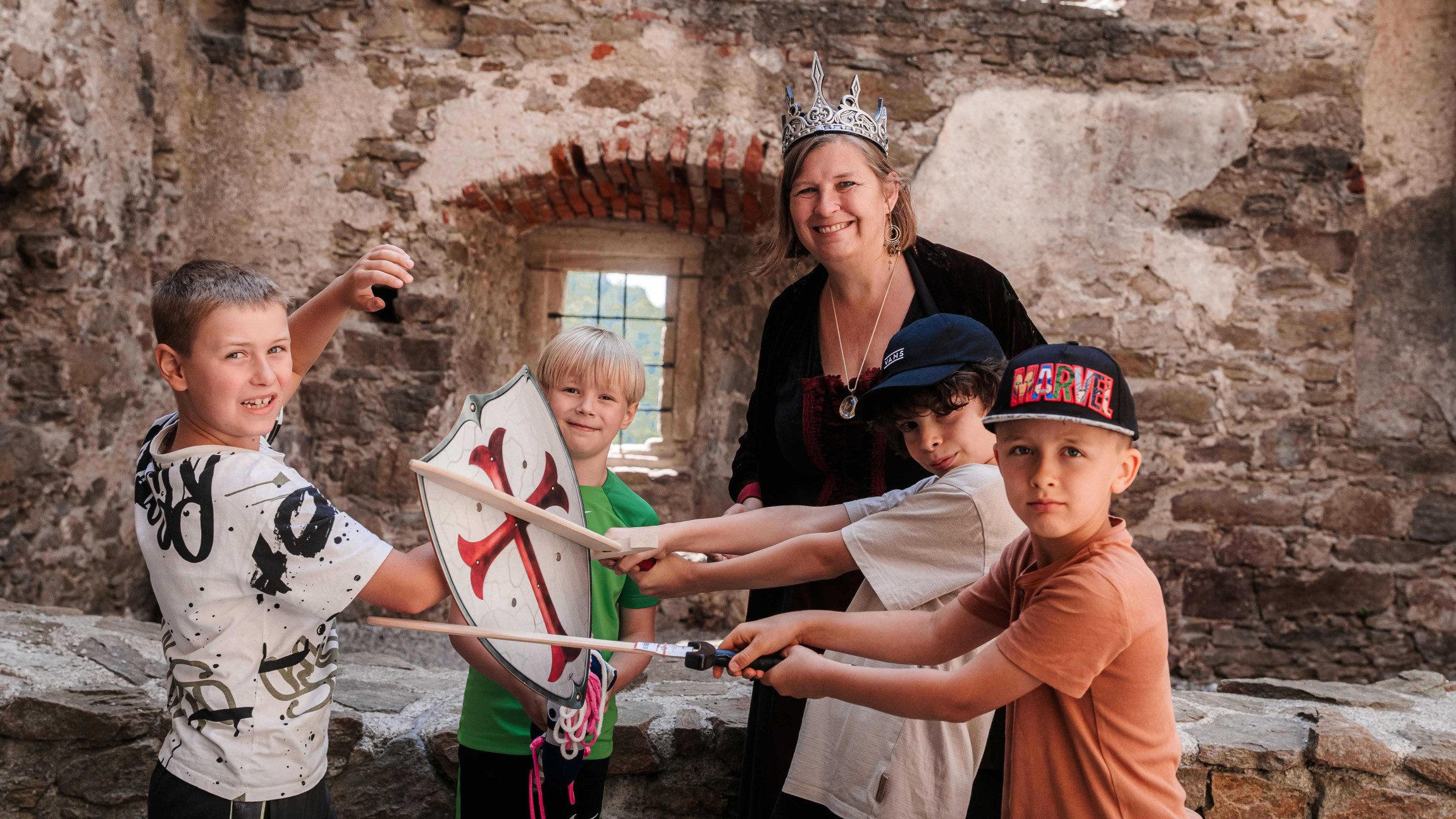 Gruppenfoto von Kindern mit Holzschwertern und einem Schild und einer Frau mit einer Krone.