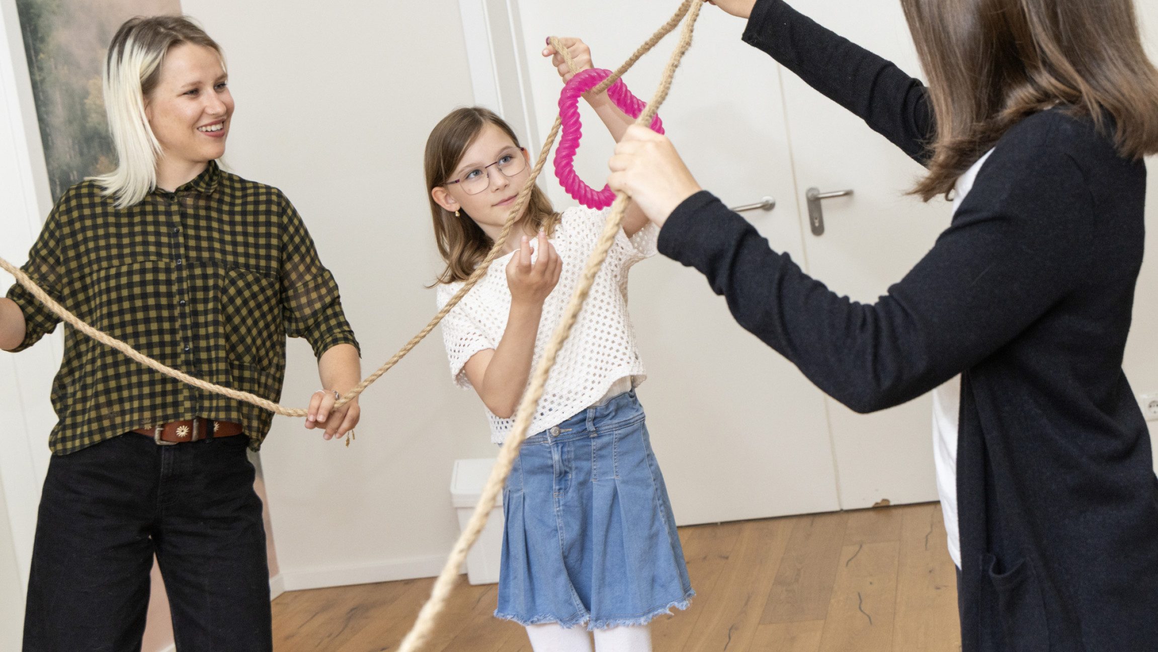 Foto von Kindern und einer Erwachsenen, die einen Reifen über ein gespanntes Seil bewegen.