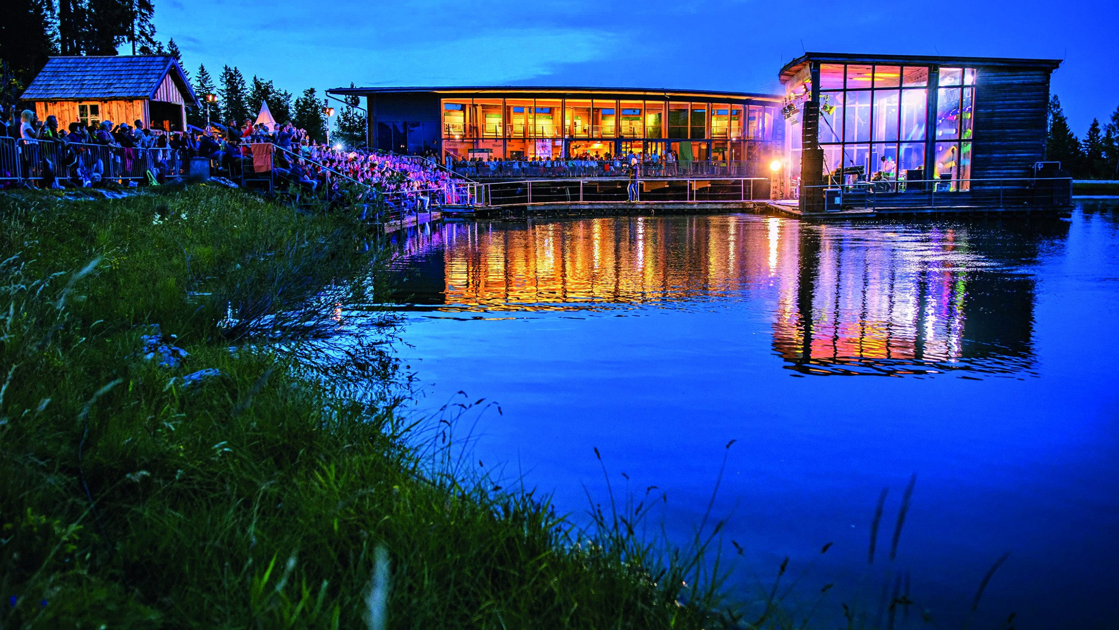 Blick auf ein beleuchtetes Gebäude über einen See hinweg.