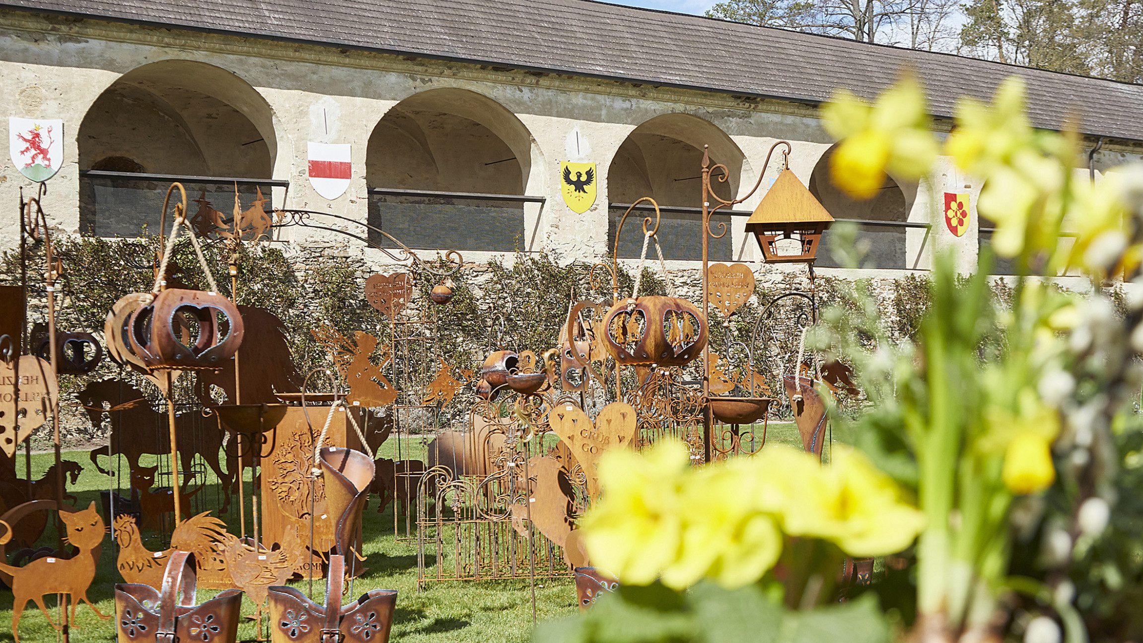Blick auf Eisenfiguren die im Innenhof der Rosenburg stehen. Im Vordergrund sind Blumen zu sehen.