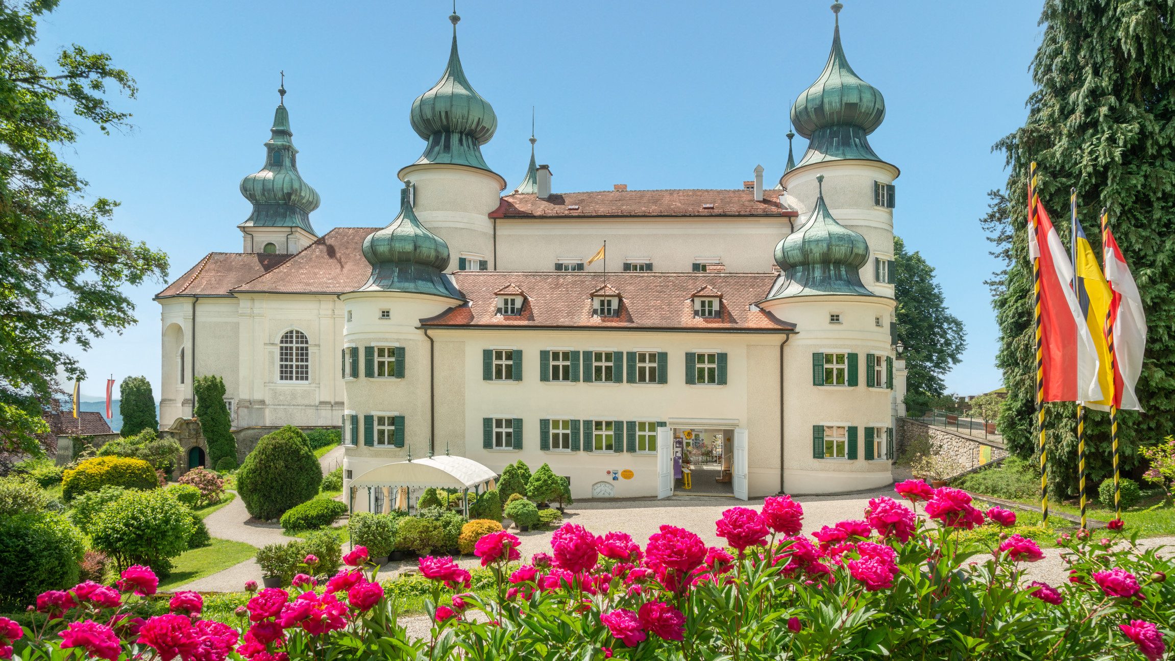 Blick auf das Schloss Artstetten vor welchem Pfingstrosen zu sehen sind.