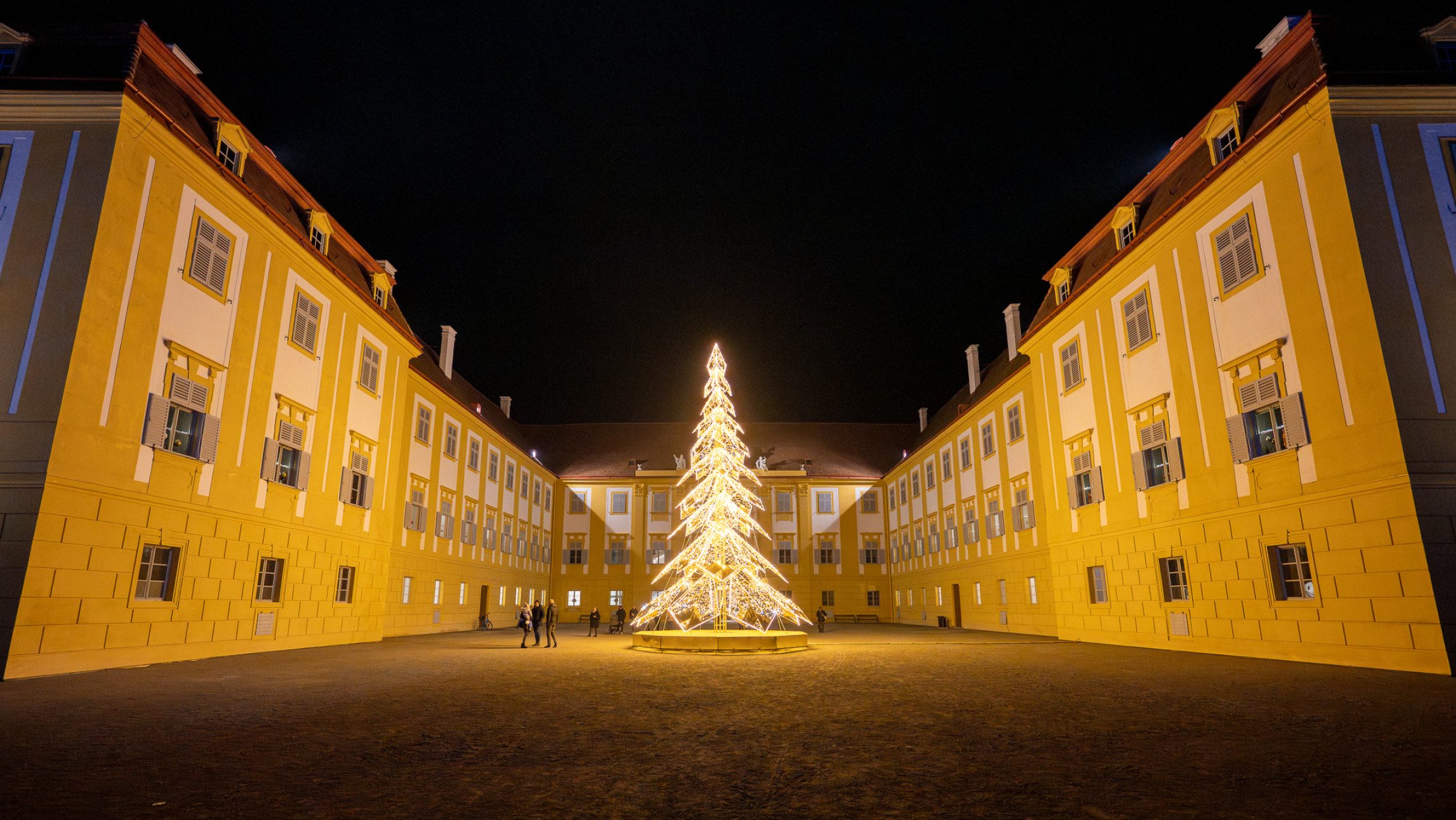Blick auf Schloss-Hof vor dem ein beleuchteter Weihnachtsbaum steht.