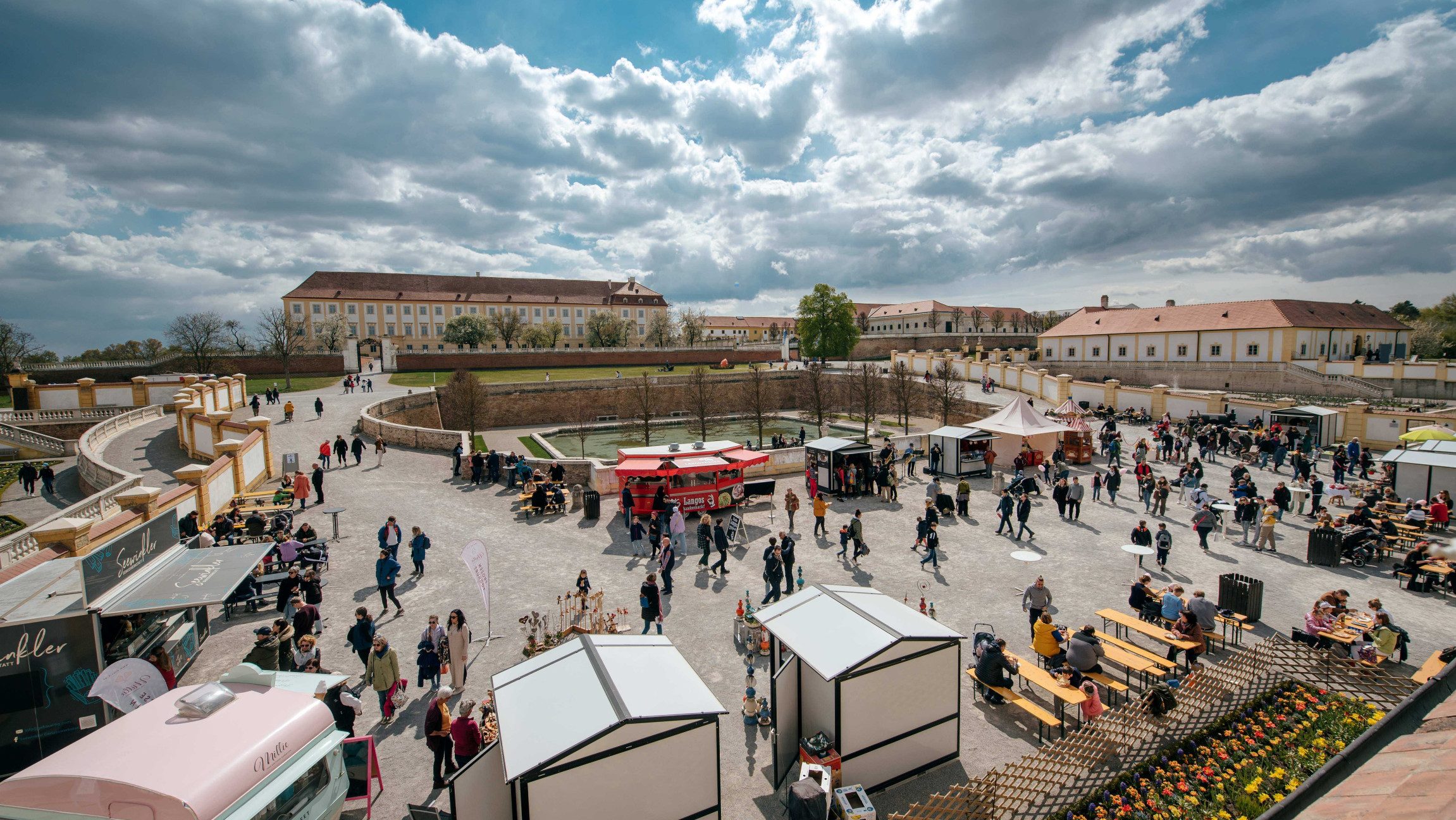 Blick auf einen Markt mit kleinen Ständen, der vor Schloss Hof aufgebaut ist und den einige Personen besuchen,