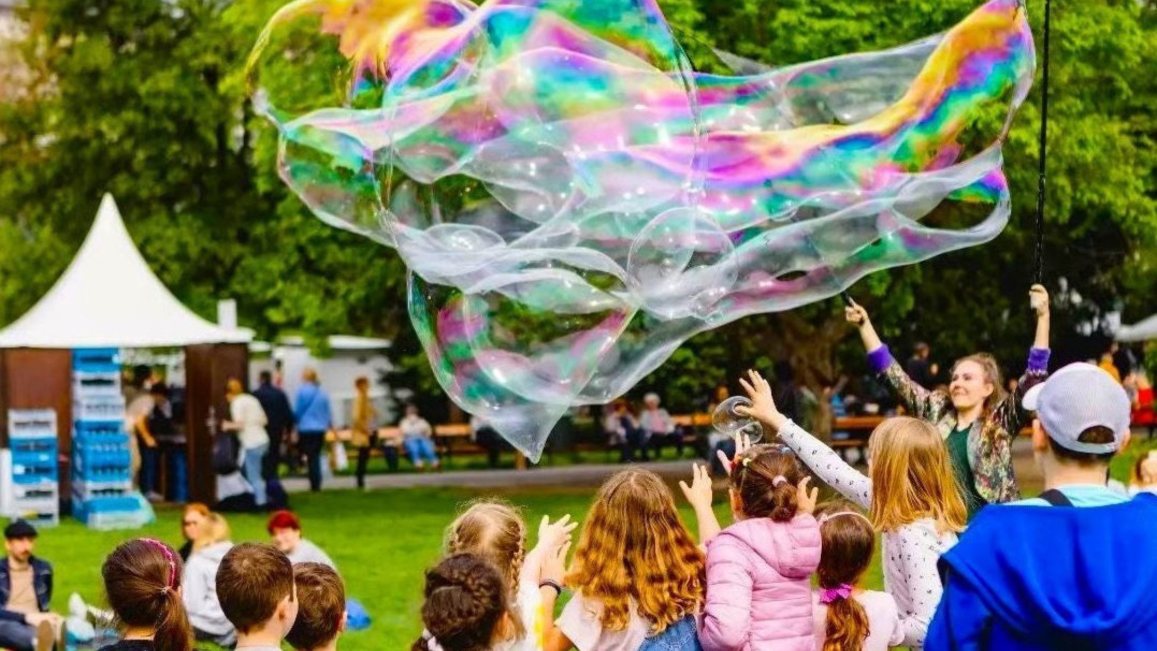 Foto von Kindern von hinten, die eine Riesenseifenblase jagen.