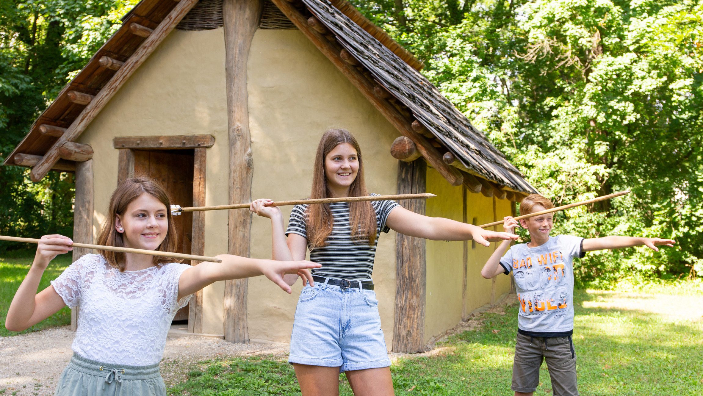 Foto von drei Kindern, die mit Speeren von einer Hütte stehen.