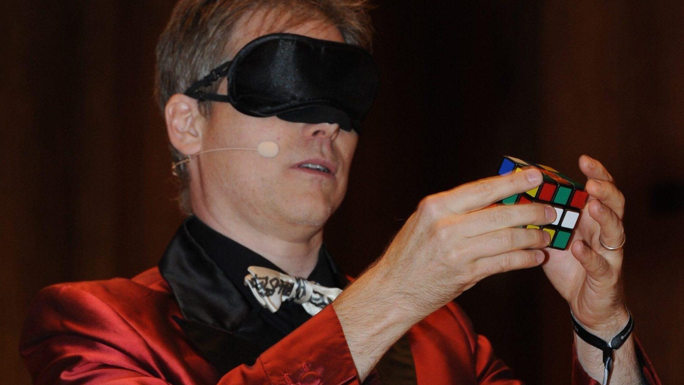 Foto von einem Mann mit verbundenen Augen der einen Zauberwürfel löst.