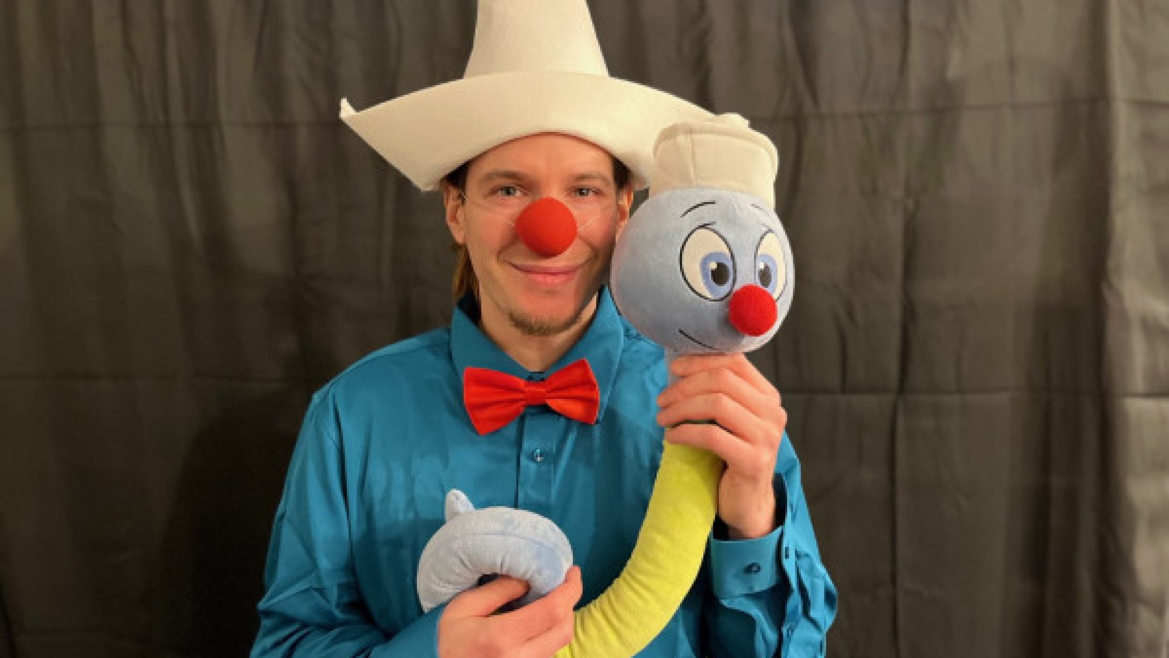 Foto von einem Clown der ein Stofftier in den Händen hält.