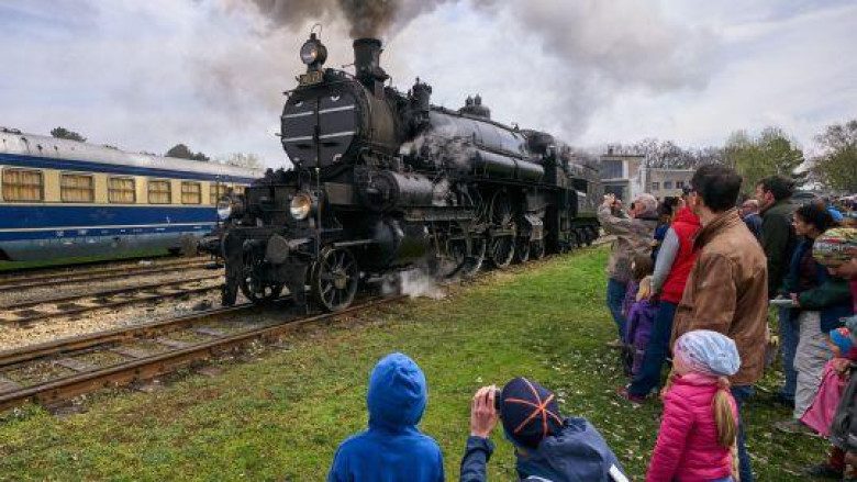 Eine Dampflock fährt und mehrere Personen stehen auf einer Wiese und schauen zu.