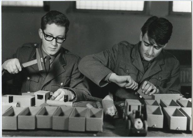 Schwarz-weiß Foto von zwei Männern in Uniform, die Spielzeug aus Holz herstellen.