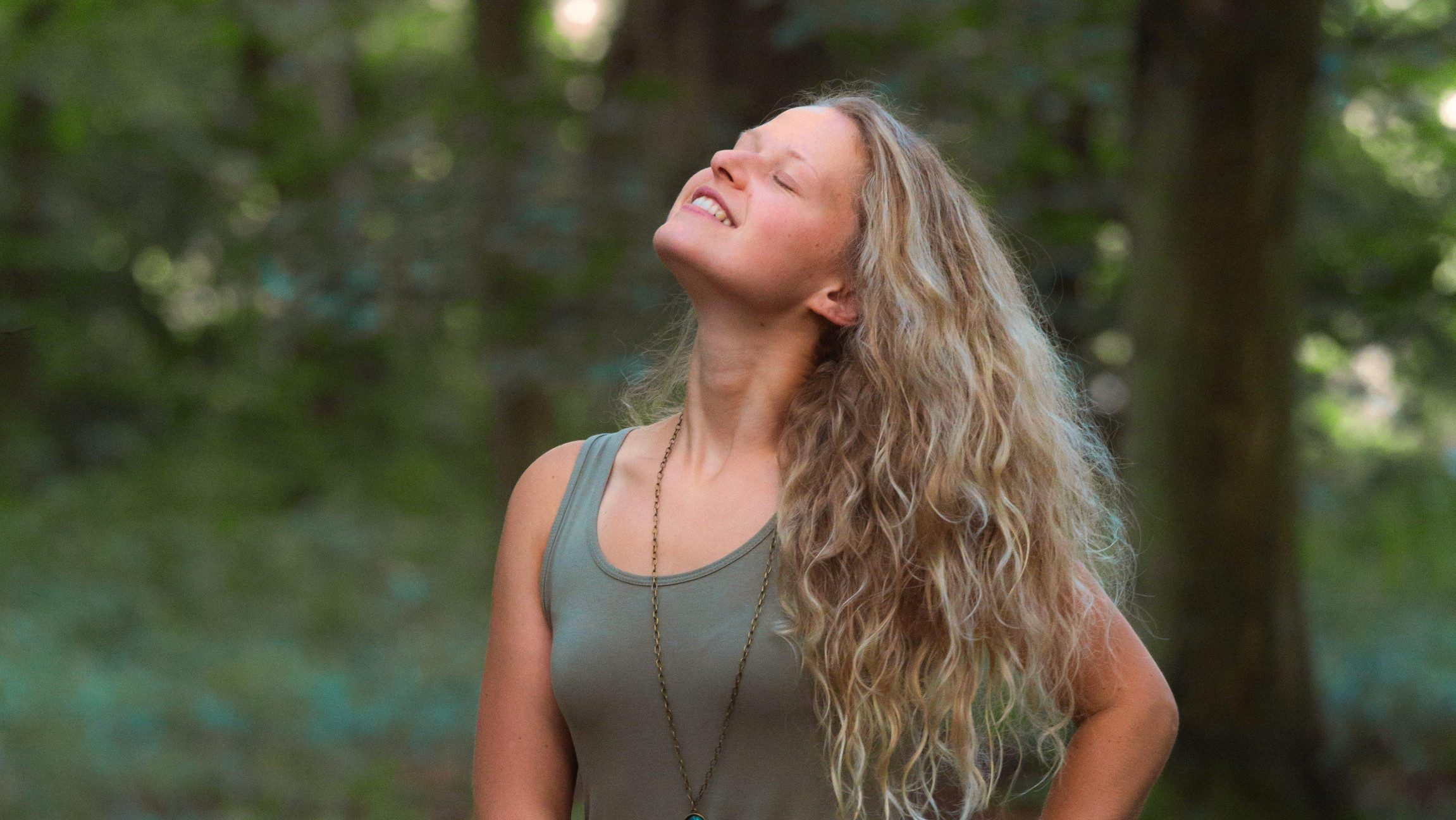 Frau mit Kopf in den Nacken gelegt mit Lächeln auf den Lippen die in einem Wald steht