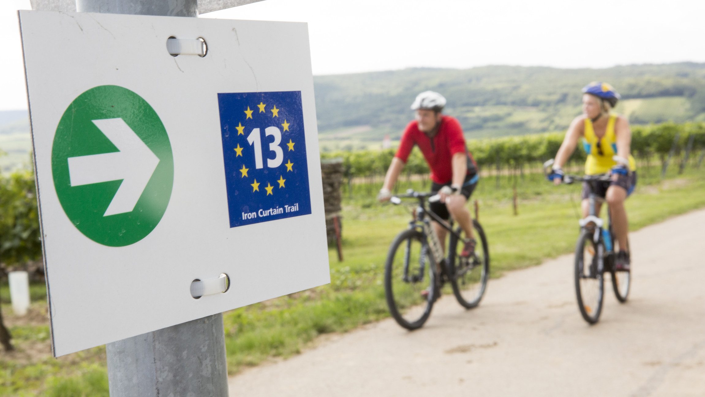 Beschilderung und Radfahrer:innen am Iron Curtain Trail