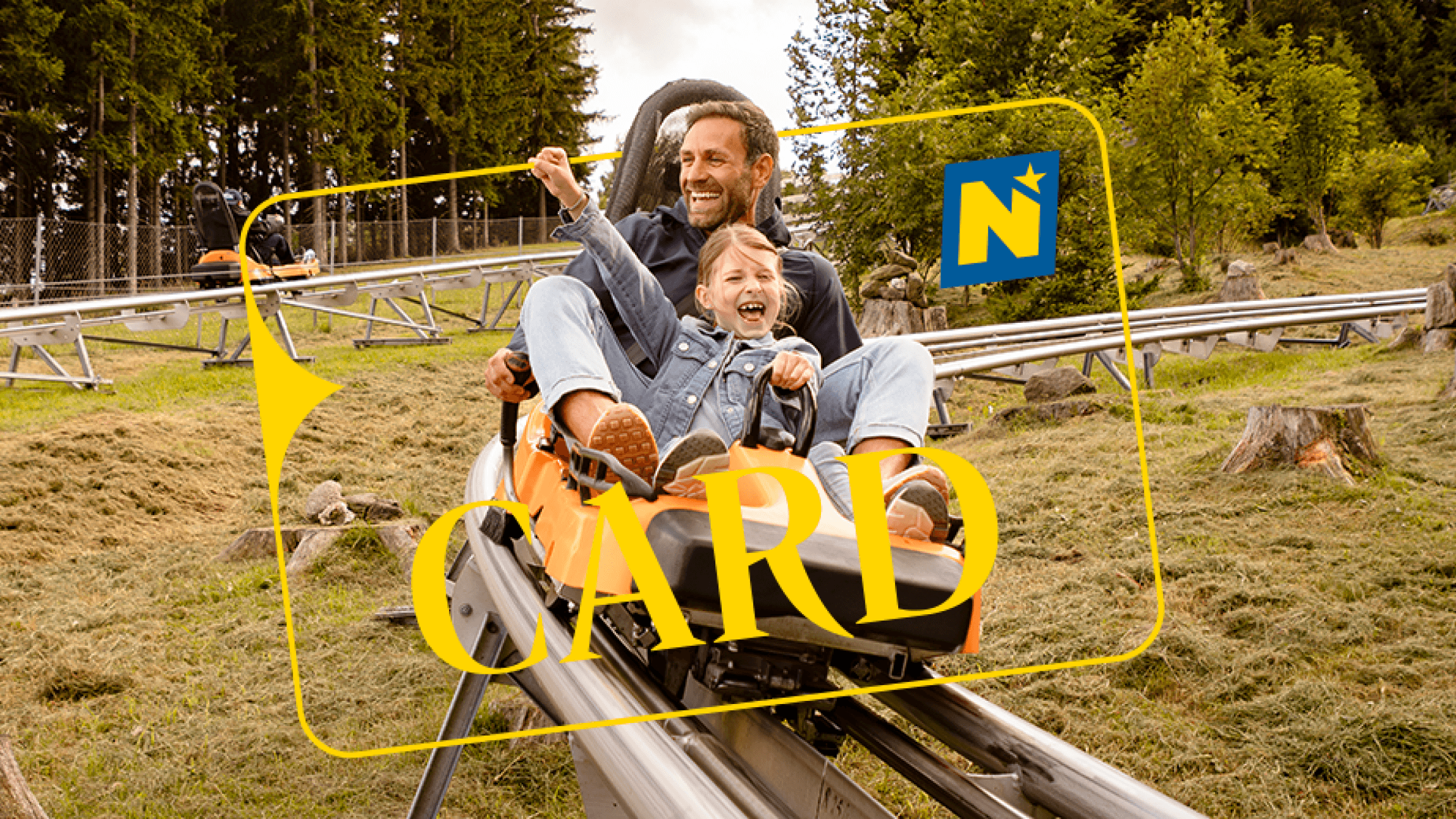 Ein Vater fährt mit seiner Tochter mit der Sommerrodelbahn