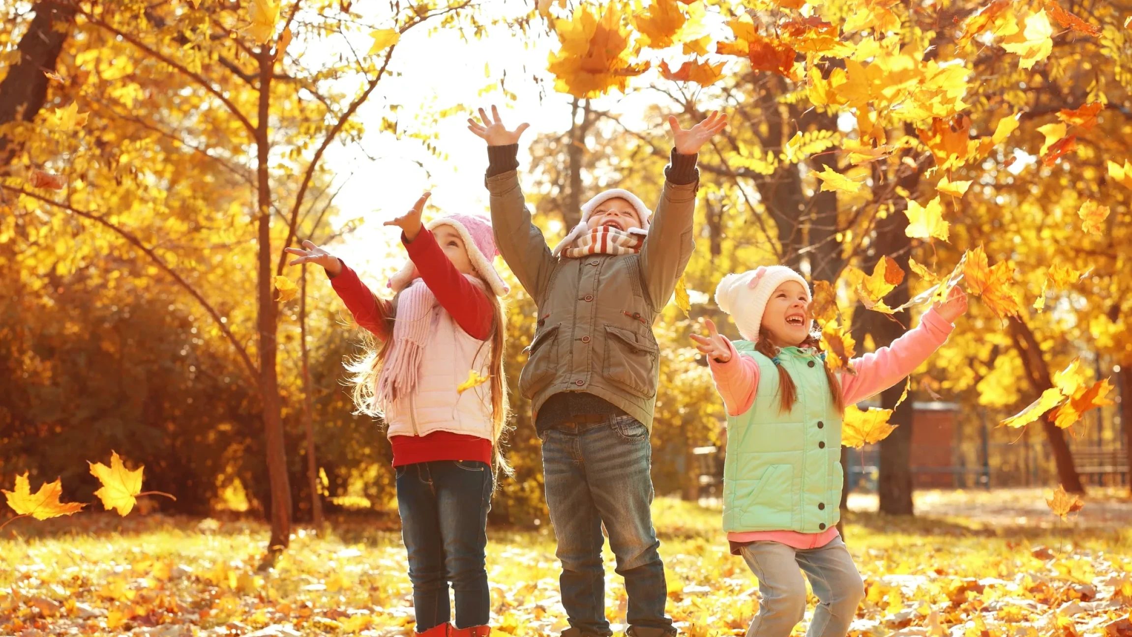Kinder erfreuen sich am Herbst und werfen buntes Laub.