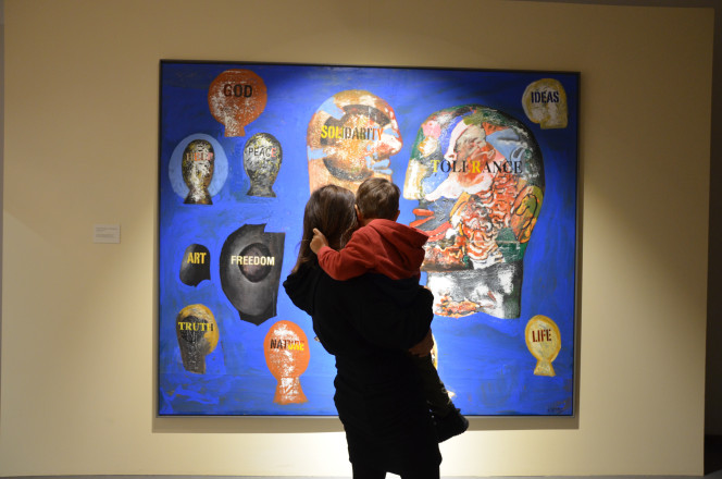 Frau mit Kind im Arm blickt auf Kunstwerk an der Wand