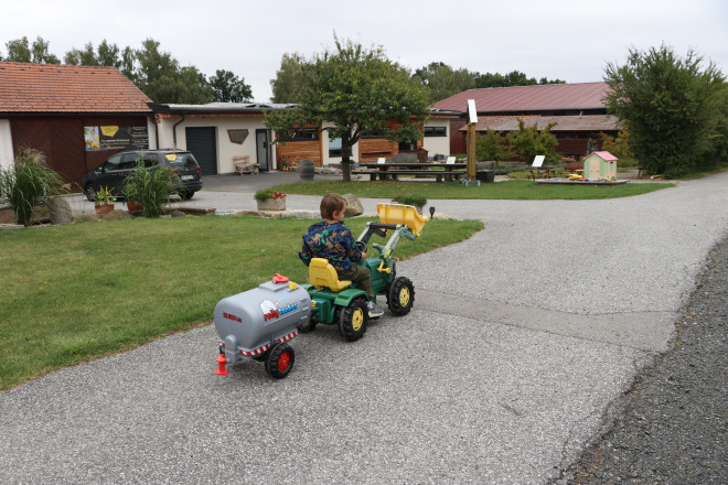ein junger Bub sitzt auf einem grünen Spielzeugtraktor und fährt durch einen Garten