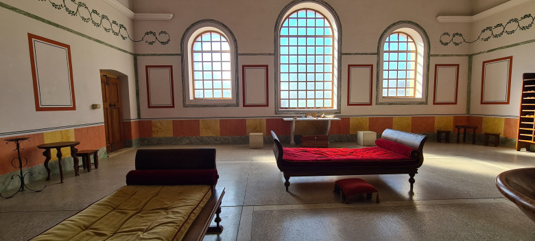 Rekonstruierter Wohnraum in der Römerstadt Carnuntum mit römischen Liegen, großen Rundbogenfenstern und farbig gestalteten Wandmalereien. Die Einrichtung vermittelt einen Eindruck vom Wohnen in der Antike.