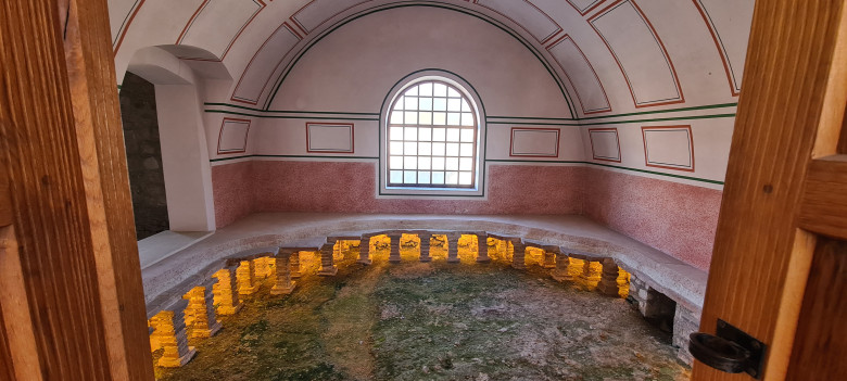 Blick in die rekonstruierte römische Therme der Römerstadt Carnuntum. Der historische Raum mit Rundbogenfenster und den Überresten der antiken Badeanlage vermittelt einen Eindruck der römischen Badekultur.