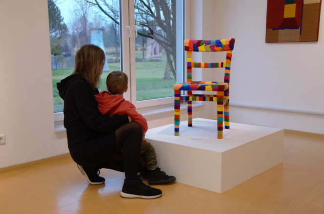 Frau und Kind betrachten bunten Stuhl als Kunstwerk