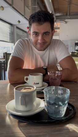 Im Vordergrund stehen zwei gefüllte Kaffeetassen und im Hintergrund sieht man den Körper eines Mannes