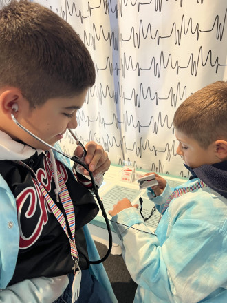 Zwei Jungs, der eine hört mir einem Stethoskop sein eigenes Herz ab, der andere probiert einen Puls-Messer aus