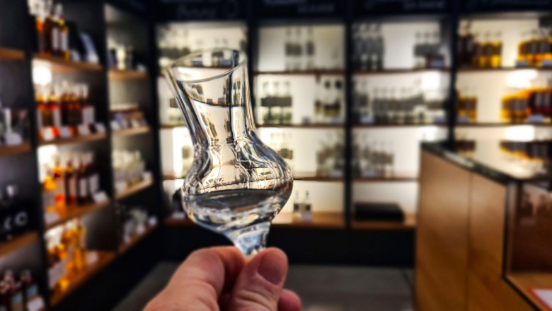 Hand hält Glas vor Shopregalen