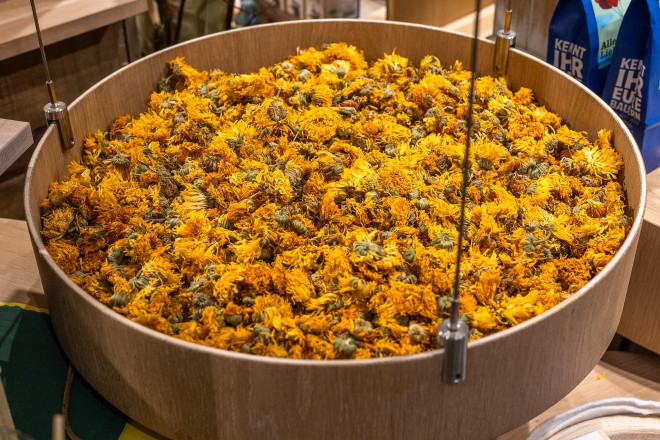 Getrocknete Ringelblumenblüten liegen in einer großen Holzschale im SONNENTOR Erlebnis. Die leuchtend gelben und orangefarbenen Blüten zeigen die Vielfalt der verwendeten Kräuter und Blüten.