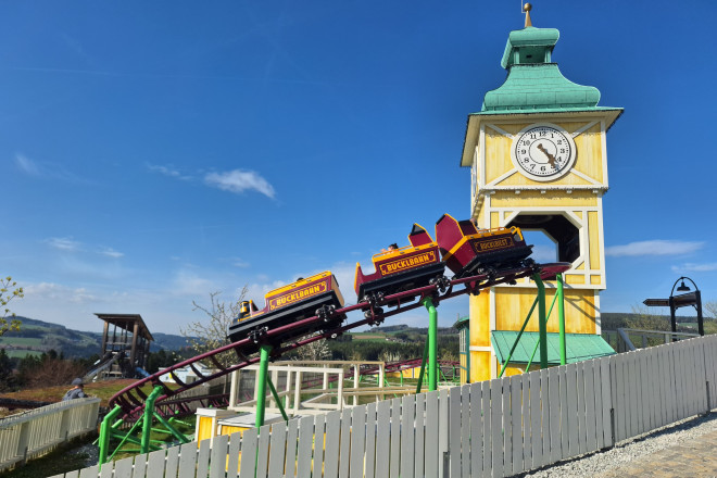 Eine Achterbahn fährt durch einen Kirchenturm im Eis-Greissler Erlebnispark