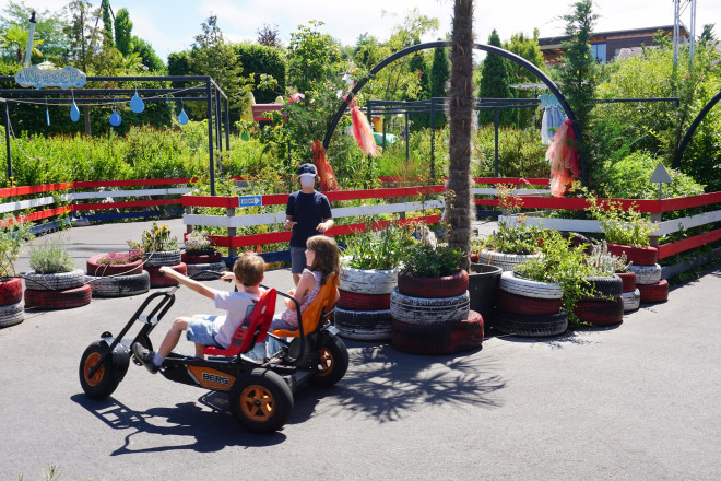 Kinder fahren mit einem Gokart durch einen abwechslungsreichen Parcours in den Kittenberger Erlebnisgärten. Farbenfrohe Pflanzen, dekorierte Gartenbereiche und Spielstationen sorgen für eine lebendige Atmosphäre.