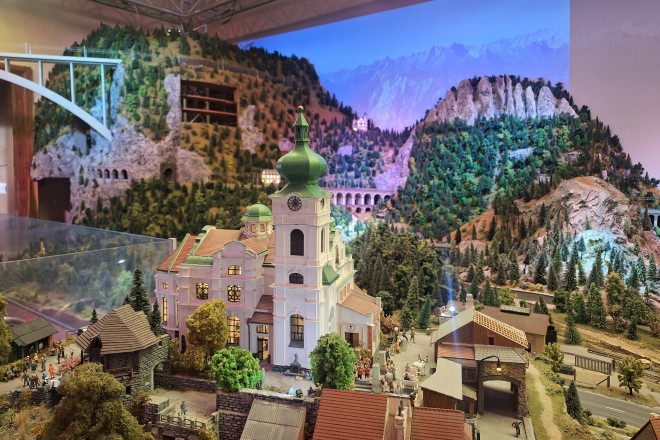 Eine detailgetreue Miniatur-Landschaft mit Kirche, Bergen, Wäldern und Eisenbahnstrecken in der Modellbahnwelt Schiltern. Die liebevoll gestaltete Szenerie bildet eine alpine Landschaft im Kleinformat nach.