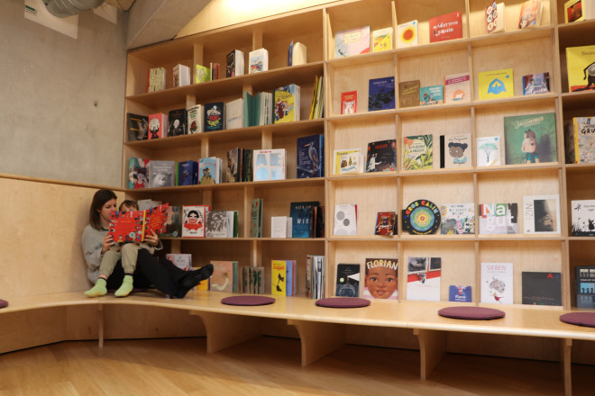 Mutter und Kind die vor einem Bücherregal sitzen und gemeinsam ein Buch lesen