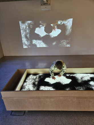 Kleiner junge Spielt in einer Kiste mit Sand auf die Licht projiziert wird