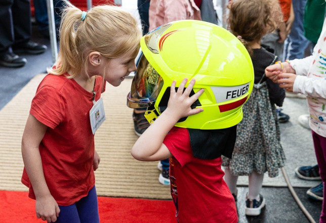 Ein Kind hat einen großen Feuerwehrhelm auf und das andere Kind sieht durch die Schutzbrille des Helms.