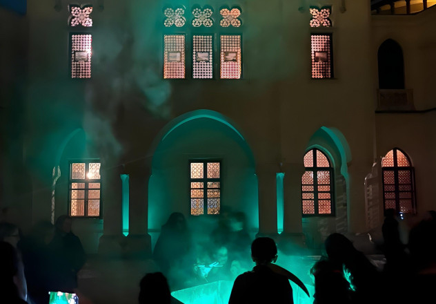Blick im dunkeln auf eine Seite vom Schloss vor der Menschen stehen und Rauch aufsteigt.
