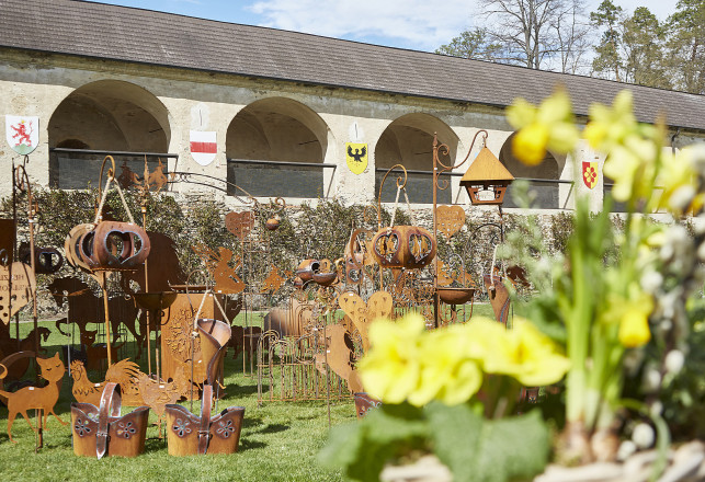 Blick auf Eisenfiguren die im Innenhof der Rosenburg stehen. Im Vordergrund sind Blumen zu sehen.
