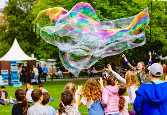 Foto von Kindern von hinten, die eine Riesenseifenblase jagen.