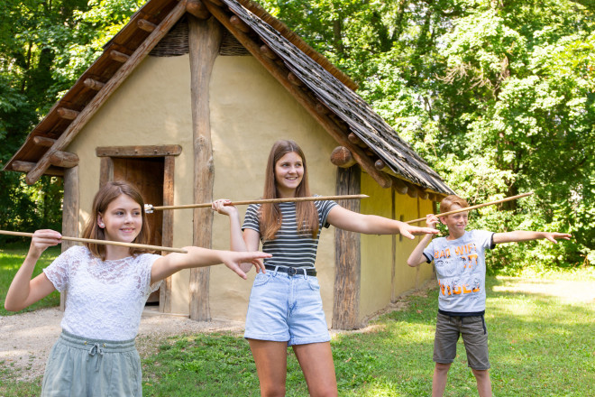 Foto von drei Kindern, die mit Speeren von einer Hütte stehen.
