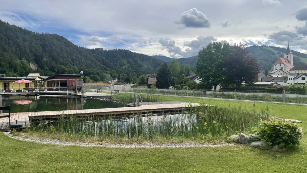 Blick auf den Naturschwimmteich und die umliegende Berglandschaft.