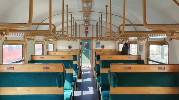 Blick in den nostalgischen Waggon mit grünen Sitzbänken aus Holz.