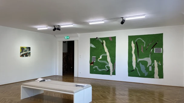 Blick durch den Ausstellungsraum auf große grüne Wandbilder.