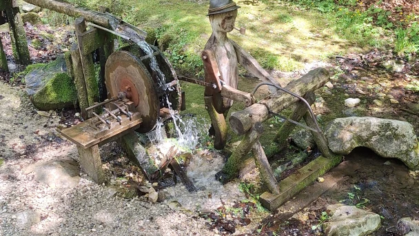 Blick auf den Wasserlauf und ein Wasserrad aus Holz mit geschnitztem Holzfäller.