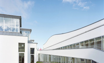 Blick auf zwei weiße moderne Gebäude mit Verglasungen, die auf einer grünen Wiese stehen.