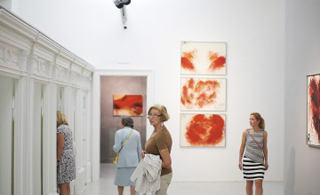 Erwachsene in einem weißen Ausstellungsraum mit Bildern an den Wänden.