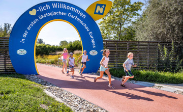 Blick auf einen blauen Bogen mit den Worten "Herzlich Willkommen" und einer Gruppe Kinder, die durchläuft