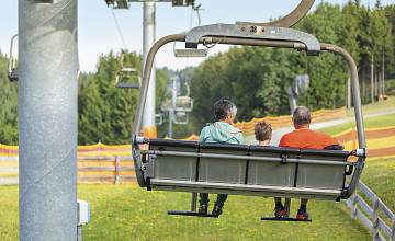 Blick von hinten auf zwei Eltern sitzen mit Ihrem Kind im 4-er-Sessellift.