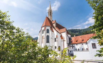 Eine weiße Kartause wird gezeigt und im Vordergrund sind Teile von Sträuchern zu sehen.