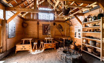 Blick in einen Raum in einer Hütte aus Holz mit Holzbalken auf der Decke und verschiedenen Möbelstücken aus Holz.